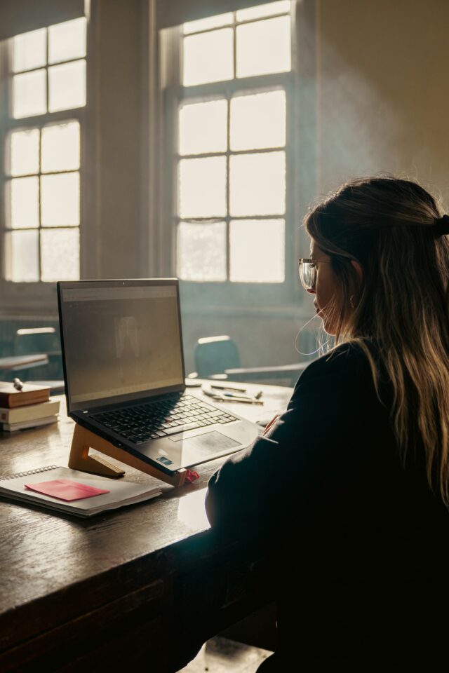 Student working on a laptop with books in a well-lit classroom
